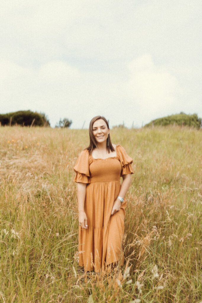 Wedding celebrant in Whakatane, Georgia stands beautifully in a field for her business portrait taken by Eilish Burt Photography