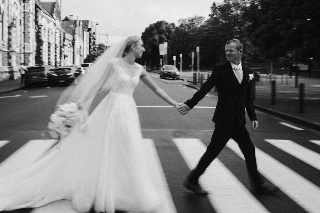 A wedding portrait of a couple walking across the street outside a Christchurch wedding venue.