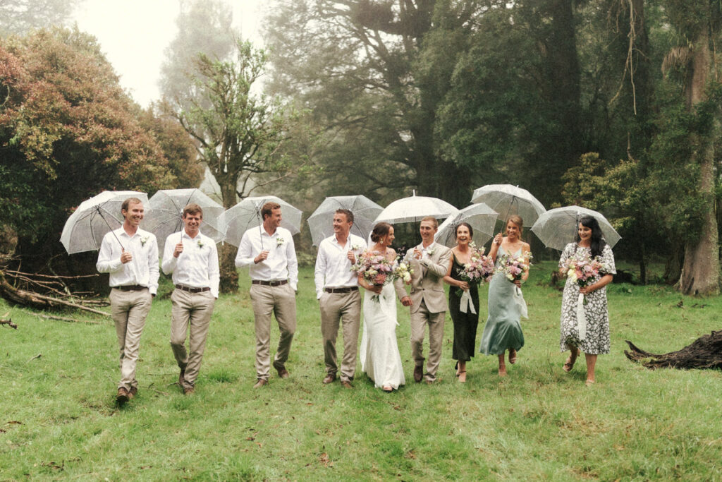 The happy bridal party hold their clear umbrellas for the couples rainy Apiti Farm Wedding. Captured by Eilish Burt Photography