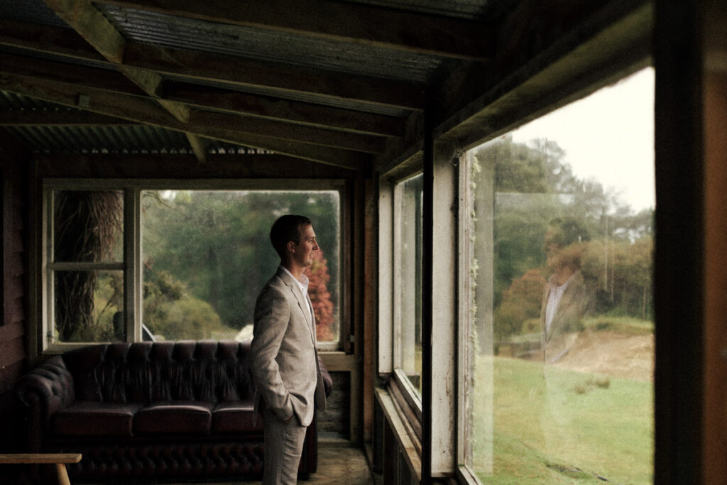 The groom anxiously looks outside as he is soon to embark on the best day of his life, marrying the love of his life. Portrait captured by Eilish Burt Photography in Apiti