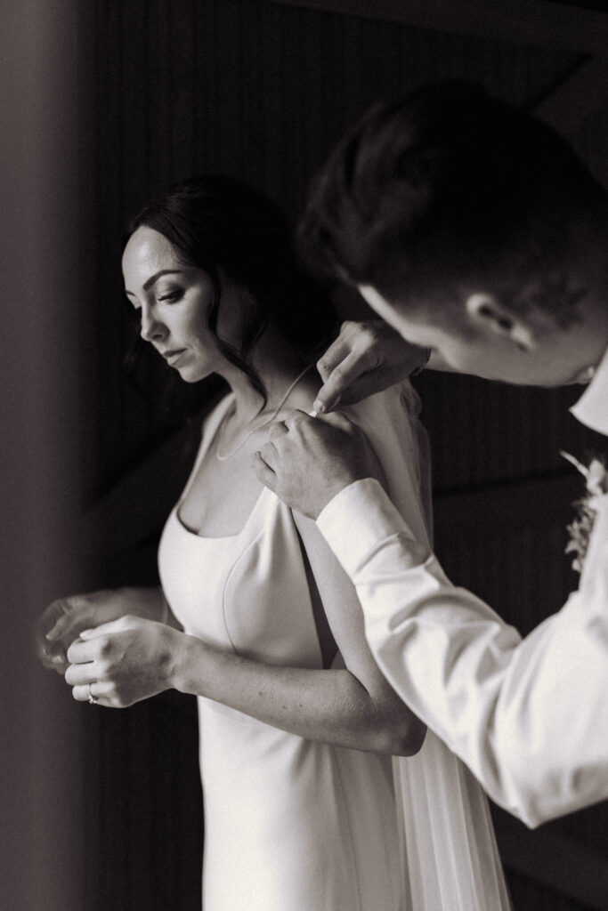 The brides twin brother does up her dress as she gets ready for the First Look with her groom in Whakatane. Taken by Eilish Burt Photography