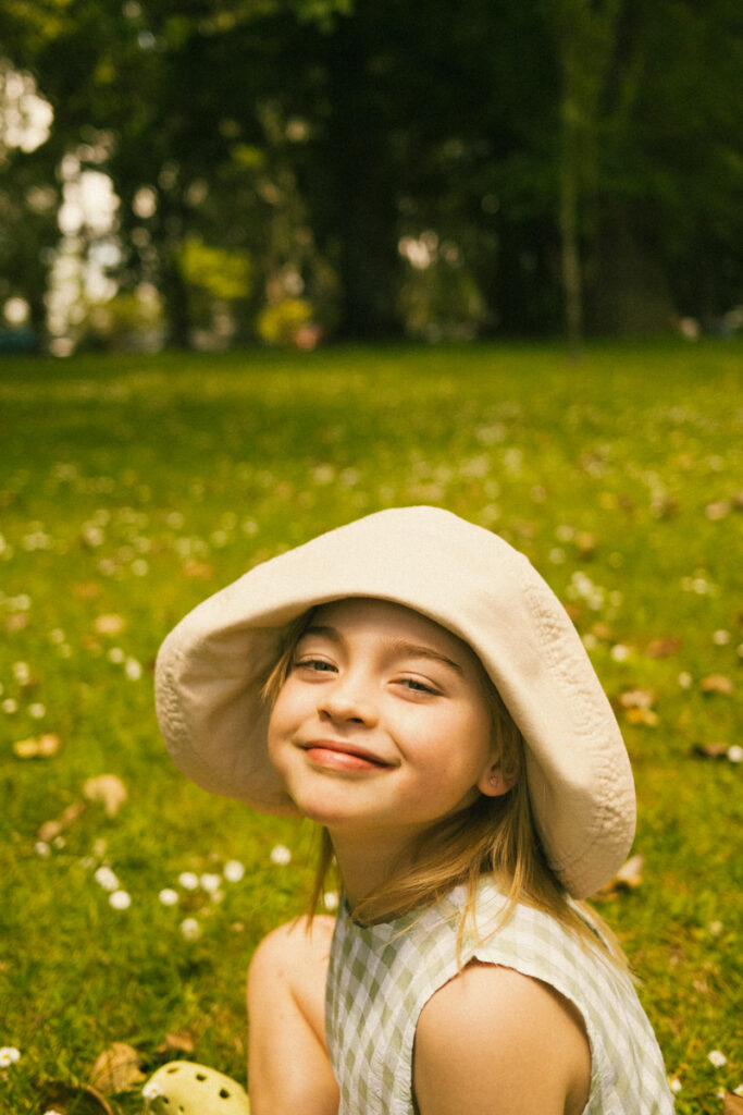 A smiley portrait of a young girl in her bucket hat in Cornwall Park, Auckland