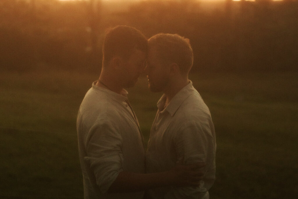 The gay wedding couple holding each other with the golden sun setting behind them in Auckland. Captured by Eilish Burt Photography