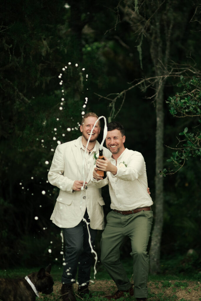 The husbands happily popping a bottle of champagne on their wedding day in Auckland. Captured by Eilish Burt Photography