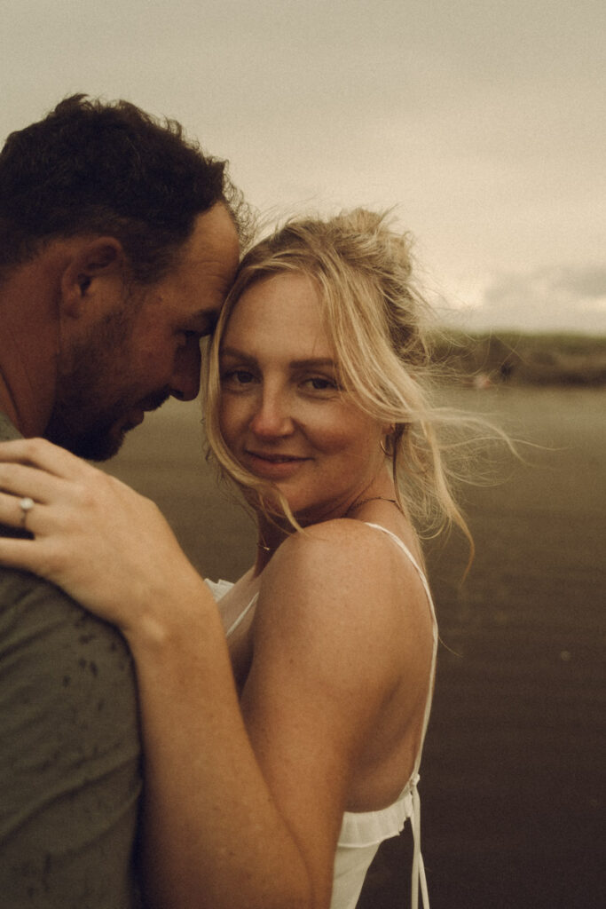 An engaged couple holding each other lovingly on the beach of Ohope, captured by Eilish Burt Photography