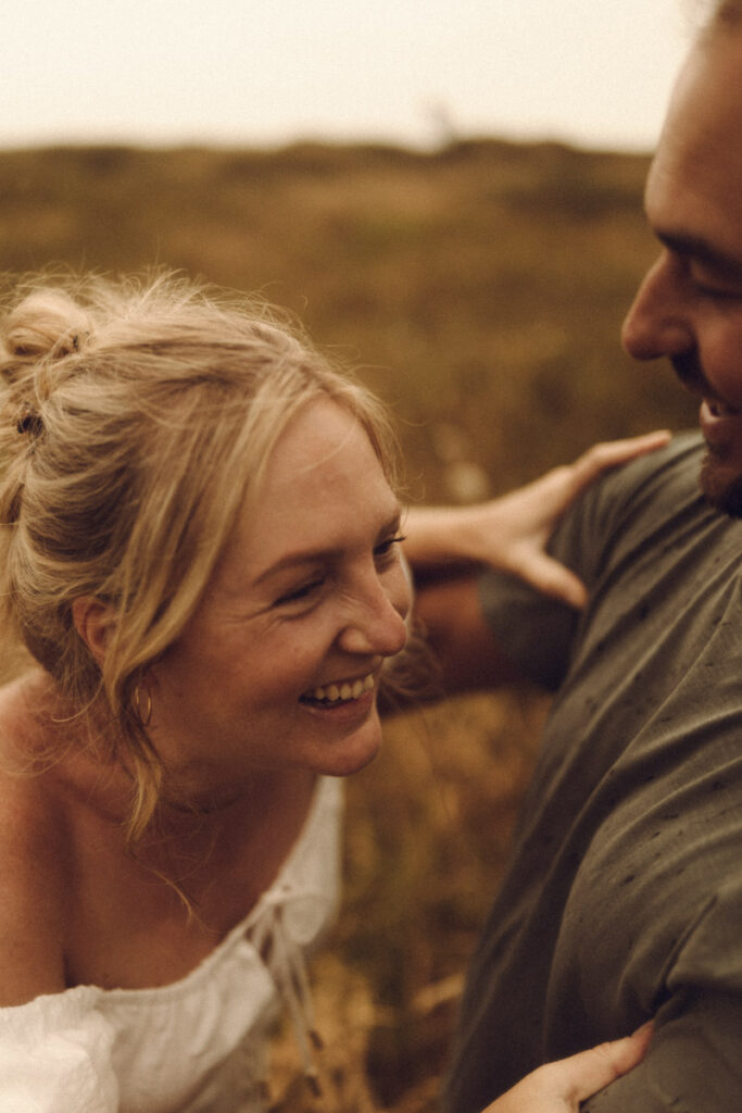 A happy engaged couple frolicking in the dunes of Ohope Beach, captured by Eilish Burt Photography