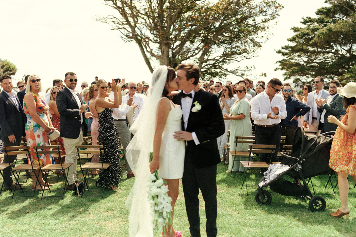 The bride and groom share a sneaky kiss under her veil at their Waiheke Wedding. Captured by Eilish Burt Photography