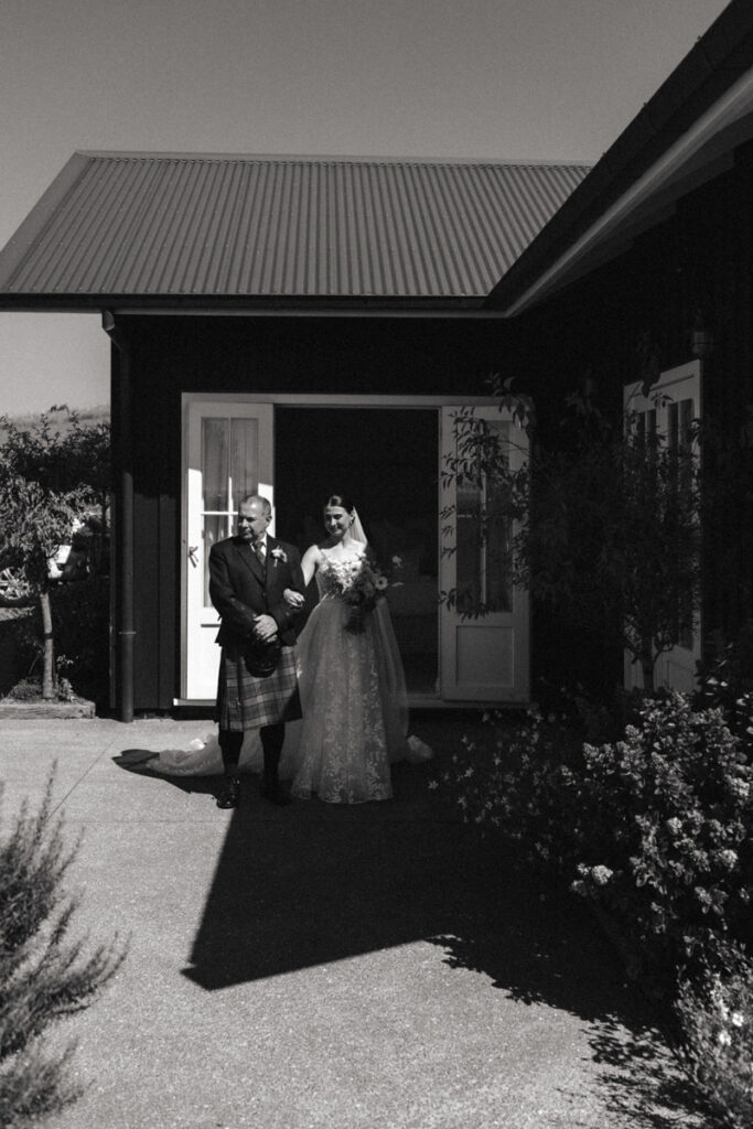 Father and bride wait patiently to walk down the aisle together. Bagpipes playing at their Mudbrick, Waiheke Wedding. Photo by Eilish Burt.