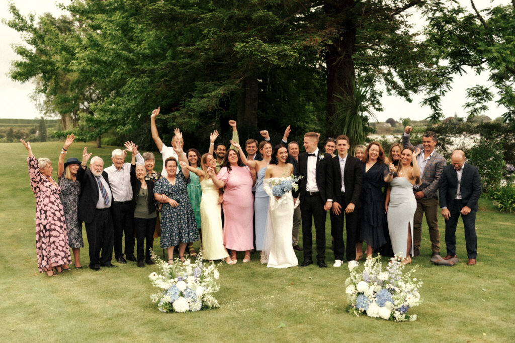 A happy wedding party cheer for the newly married couple on the lawn of Te Puna Point Retreat, Tauranga.
