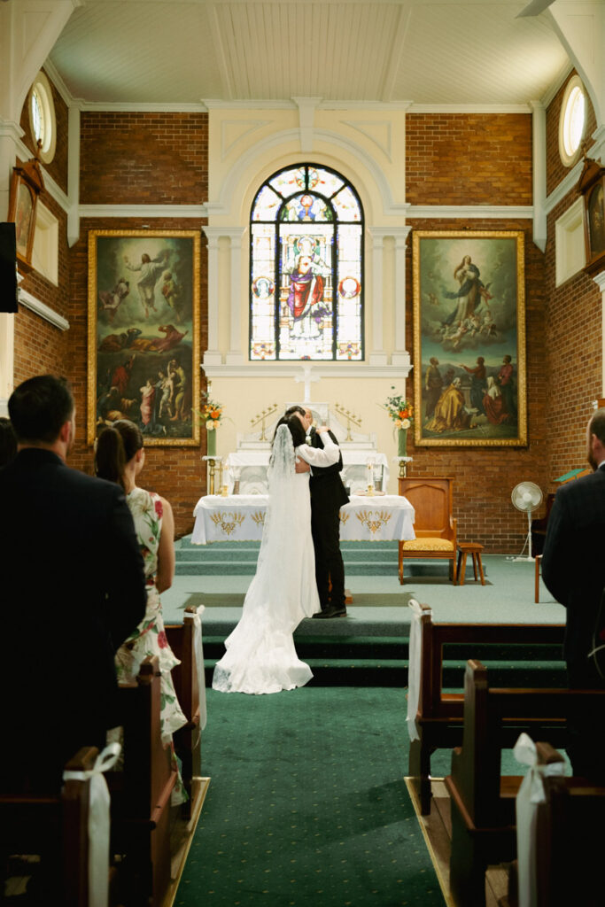 A wedding portrait of a couple sharing their first kiss inside the Catholic Church in Brisbane, Australia. Captured by Eilish Burt Photography.