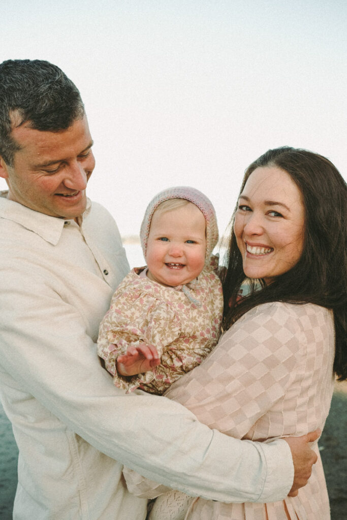 Baby gives Eilish a big smile in her family portrait with mum and dad at Ohope beach.