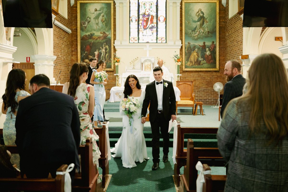 A bride and groom walk down the aisle as husband and wife. Photographed by Eilish Burt at a Catholic Church in Brisbane, Australia.