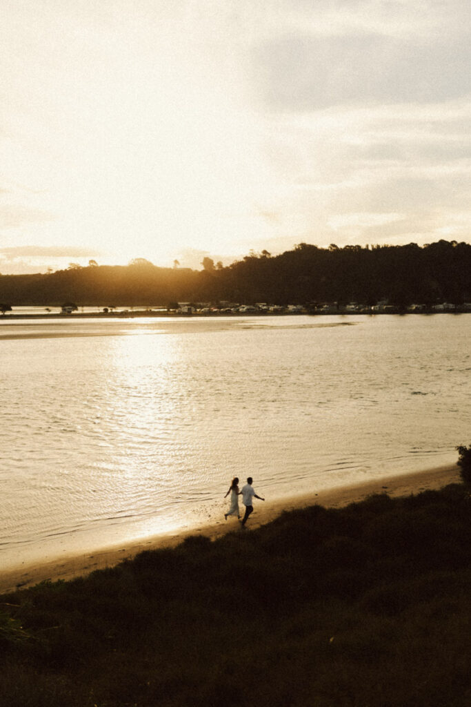 A wedding couple running along the sand of Bay of Plenty.