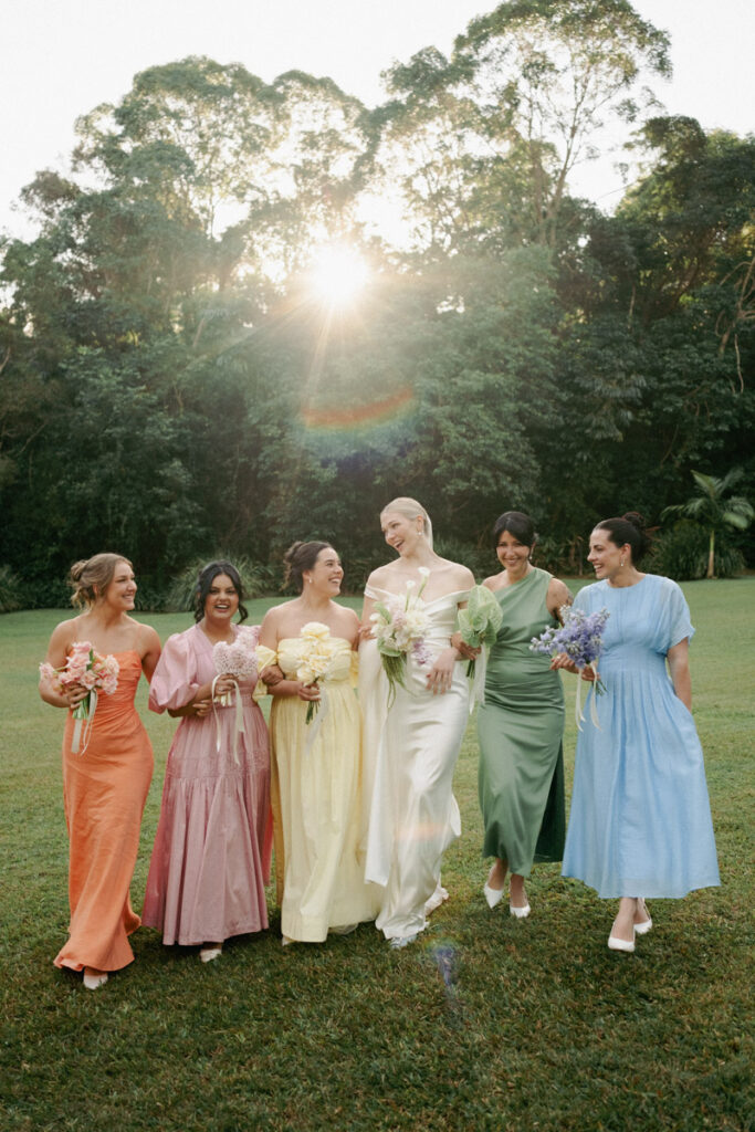 The bride and her bridesmaids walk arm in arm with the sunlight beaming through the background at Palm Creek Estate in Brisbane