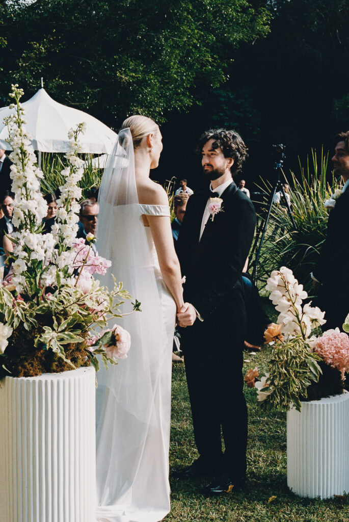 A film wedding portrait of the bride and groom at the end of the aisle holding hands.